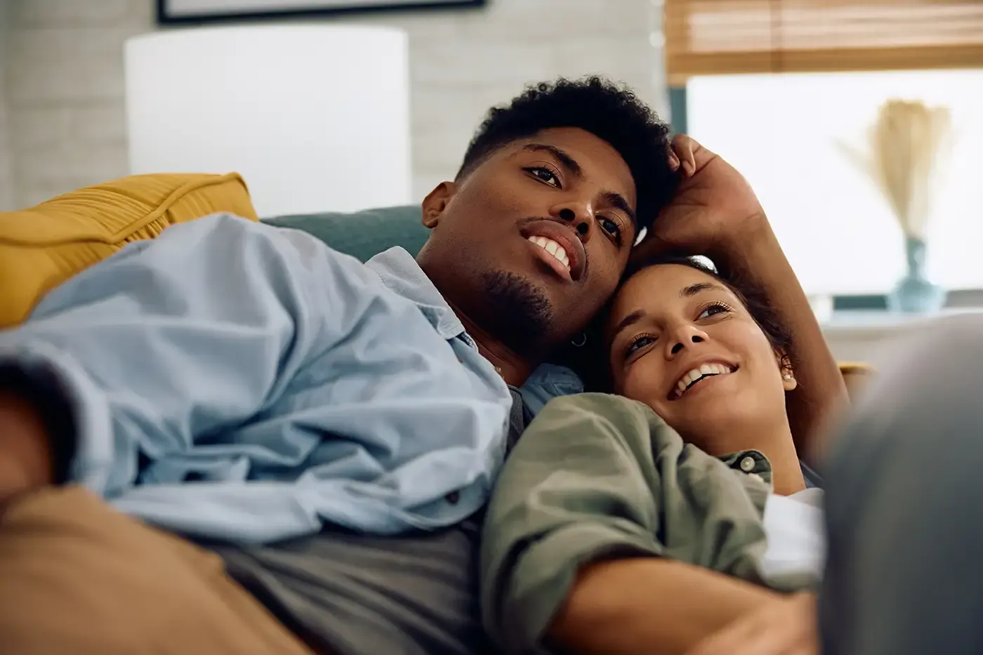 Foto de una joven pareja multirracial viendo televisión mientras están acostados en el sofá.