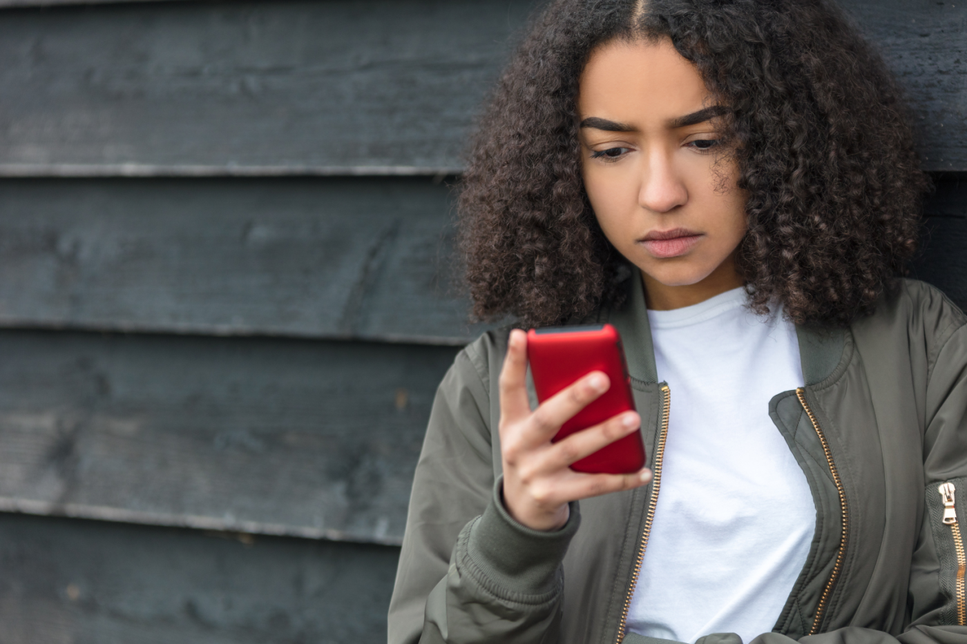 Woman leaning against wall, looking at cell phone
