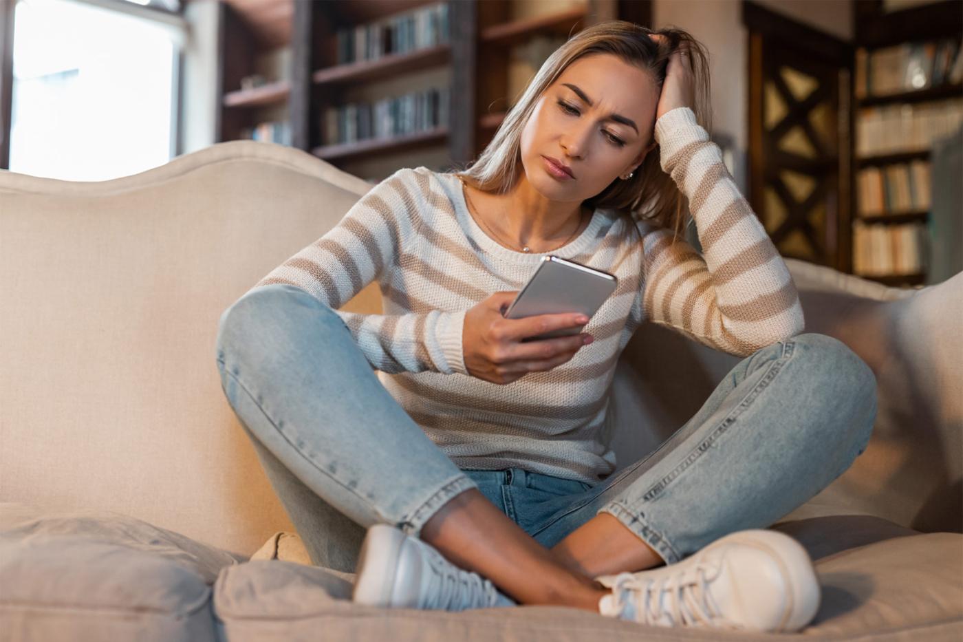 Mujer con expresión de preocupación mirando su teléfono mientras busca ayuda y apoyo inmediato.
